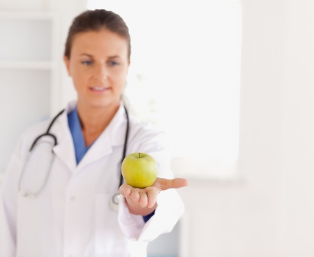 Good looking brunette doctor with stethoscope looking at an apple in the surgeryの写真素材