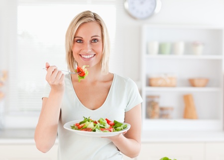 Close up of a gorgeous woman eating salad in the kitchenの写真素材