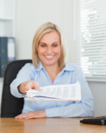 Smiling blonde businesswoman passing a paper looking at it in her officeの写真素材