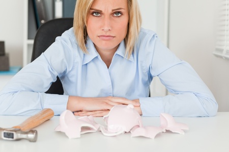 Sad woman sitting in front of an empty shattered piggy bank in her officeの写真素材