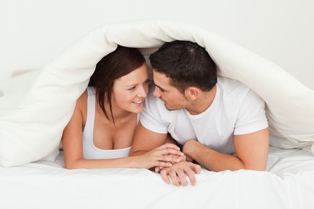 Happy couple hiding under a blanket in a bedroom