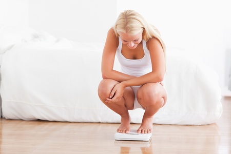Fit woman on a weighing machine in her bedroom