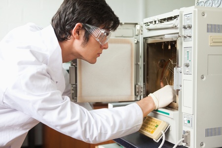 Male scientist using a laboratory chamber furnace wearing glasses