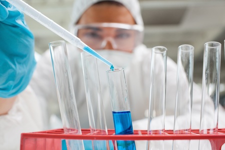 Protected science student dropping blue liquid in a test tube in a laboratory