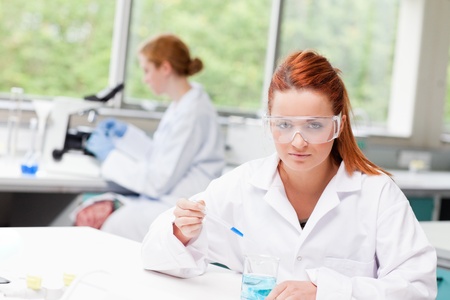 Science student dropping blue liquid in a beaker while looking at the cameraの写真素材