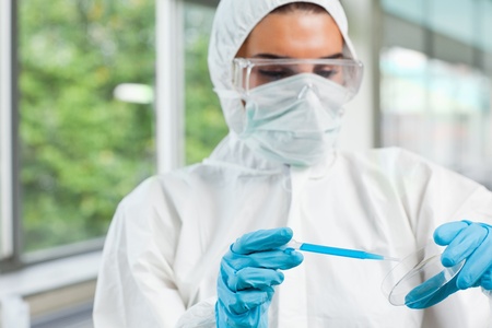 Protected female science student dropping blue liquid in a Petri dish in a laboratory