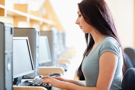 Gorgeous student working with a computer in an IT roomの写真素材