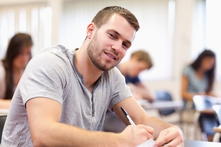 Smiling young adult writing in a classroomの写真素材