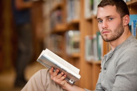 Serious male student holding a book in a libraryの写真素材