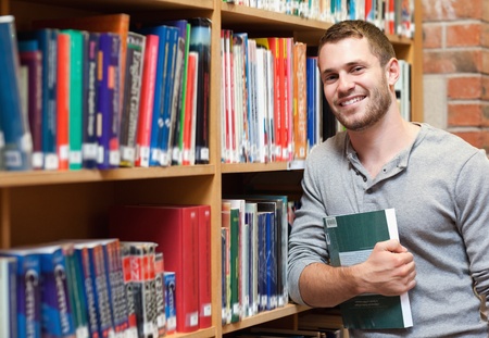 Smiling male student holding a book in a libraryの写真素材