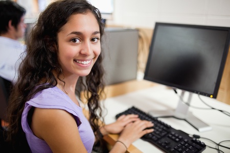 Smiling brunette student posing with a computer in an IT roomの写真素材