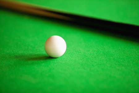 Close up of a queue ball and a queue against a green background