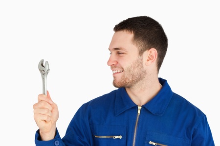 Smiling young mechanic in boiler suit looking at his wrench against a white backgroundの写真素材