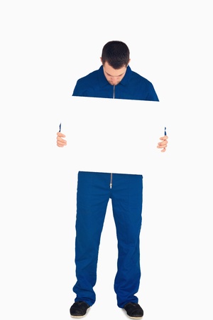 Young mechanic in boiler suit looking on banner in his hands against a white backgroundの写真素材