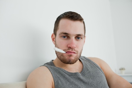 Sick man posing with thermometer in his bedroomの写真素材