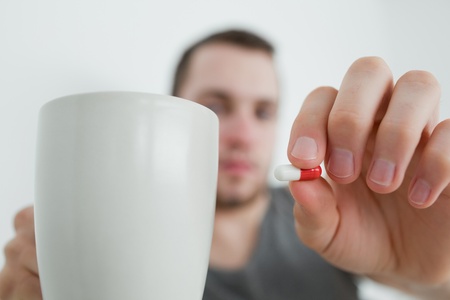 Man showing a pill and and a mug in his bedroomの写真素材
