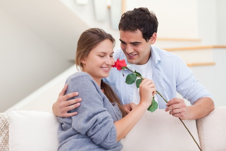 Young man offering a rose to his fiance in their living roomの写真素材