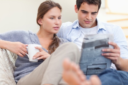 Couple reading the news while lying on a sofaの写真素材