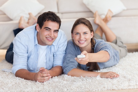 In love couple watching TV while lying on a carpetの写真素材