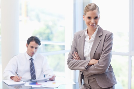 Smiling businesswoman posing while her colleague is working in a meeting roomの写真素材