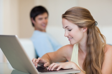 Woman using a laptop while her husband is sitting on a sofa in their living roomの写真素材