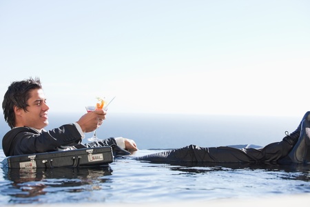 Young businessman relaxing in a swimming pool with a cocktail in a suitの写真素材