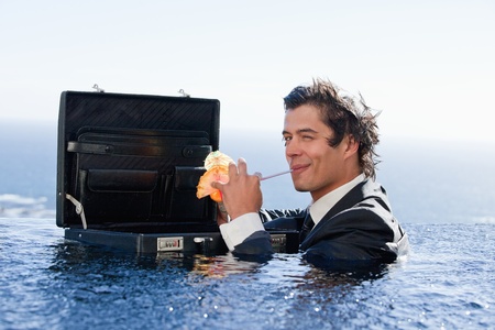 Businessman drinking a cocktail in a swimming pool