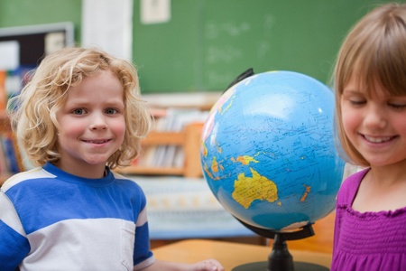 Young pupils posing in front of a globe in a classroomの写真素材