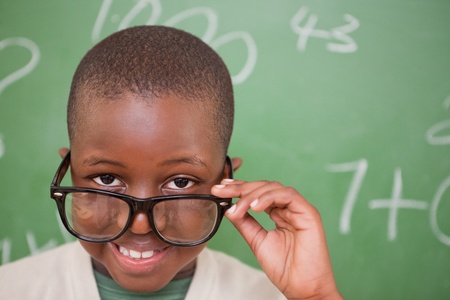 Smiling schoolboy looking over his glasses in front of a blackboardの写真素材