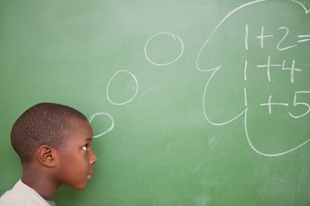 Schoolboy thinking about additions in front of a blackboardの写真素材