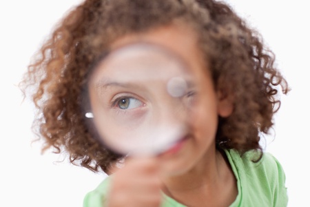 Smiling girl looking through a magnifying glass against a white backgroundの写真素材