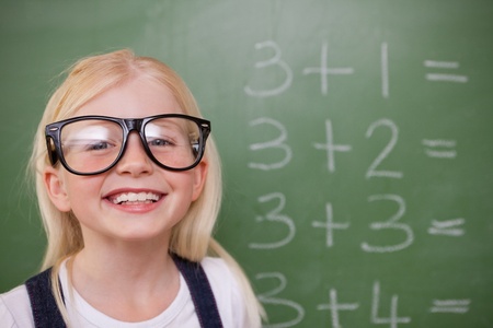 Smart schoolgirl posing in front of a blackboard in a classroomの写真素材