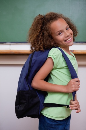 Portrait of a schoolgirl showing her backpack in a classroomの写真素材