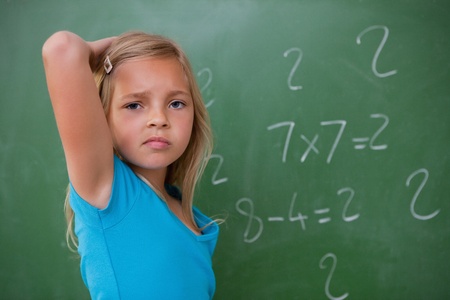 Schoolgirl thinking while scratching the back of her head in front of a blackboardの写真素材