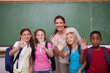 Schoolteacher and her pupils waving at the camera in a classroomの写真素材