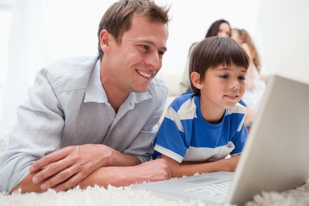 Son and father using laptop together on the carpetの写真素材