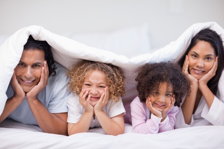 Young family hiding under the bed coverの写真素材
