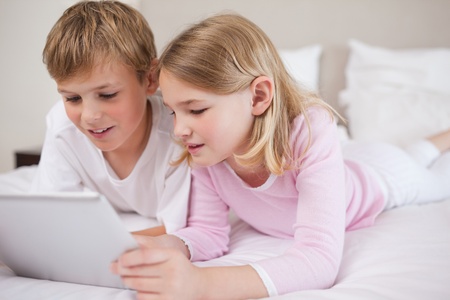 Siblings using a tablet computer in a bedroomの写真素材