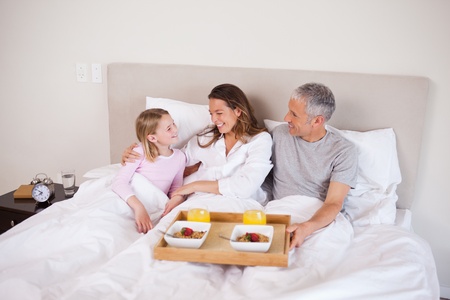 Girl having breakfast with her parents in their bedroomの写真素材