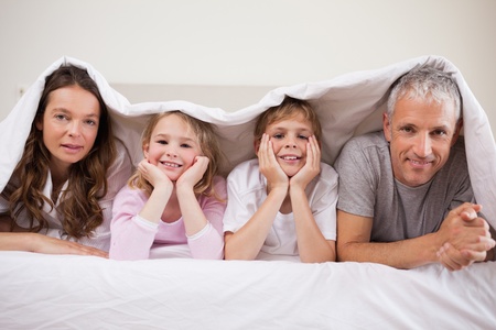 Family lying under a duvet in a bedroomの写真素材