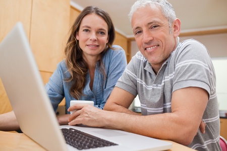 Couple using a laptop while having tea in their kitchenの写真素材