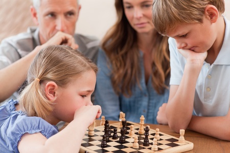 Focused children playing chess in front of their parents in a living roomの写真素材
