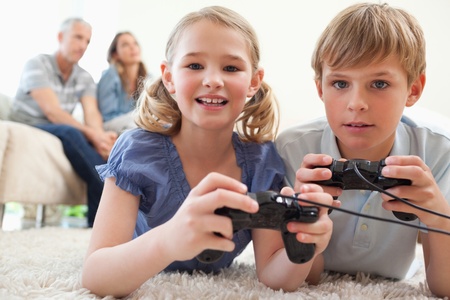 Playful siblings playing video games with their parents on the background in a living roomの写真素材