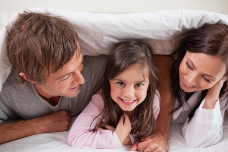 Cheerful family lying under a duvet in a bedroomの写真素材