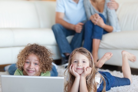 Cute children using a laptop while their parents are watching in their living roomの写真素材
