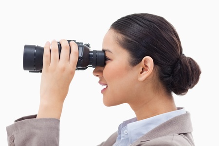 Side view of a businesswoman looking through binoculars against a white backgroundの写真素材