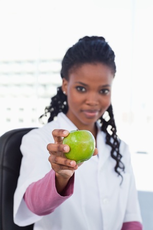Portrait of a female doctor showing an apple in her officeの写真素材
