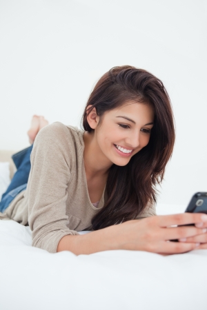 A close up shot of a woman smiling and using her phone as she lies on the bed.の写真素材