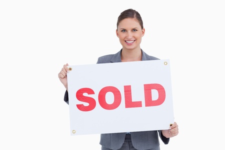 Smiling real estate agent presenting sold sign against a white backgroundの写真素材