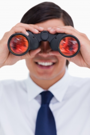 Close up of smiling tradesman looking through binoculars against a white backgroundの写真素材